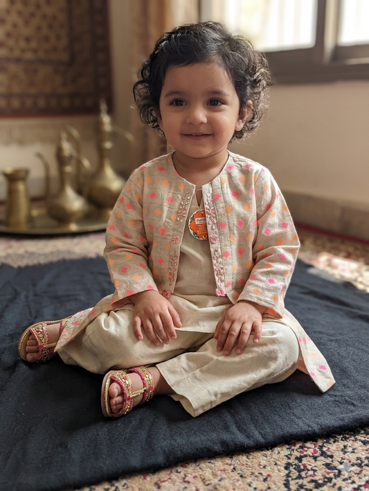 Girls light cream jacket with pink, orange, and gold geometric embroidery and beaded trim, layered over a solid off-white tunic and matching pleated wide-leg trousers,